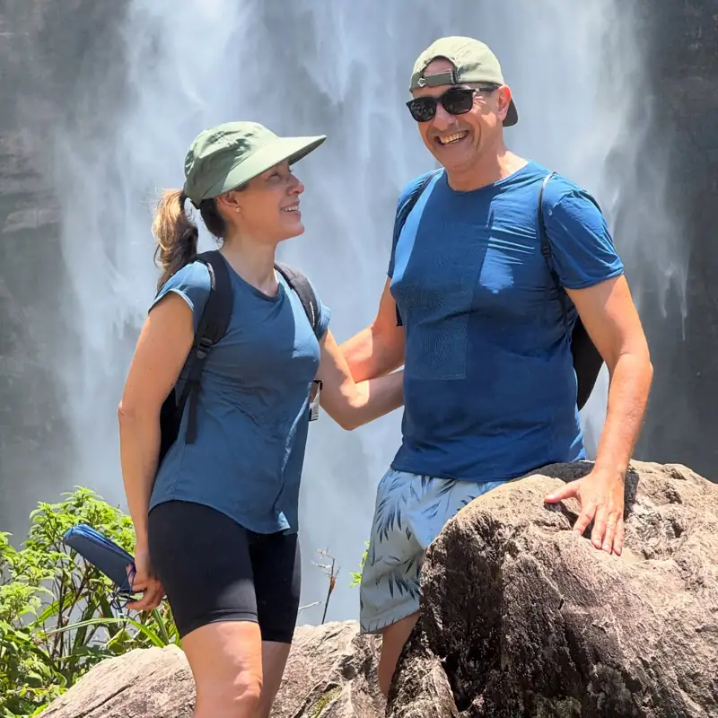 Casal de trilheiros sorrindo diante de uma cachoeira